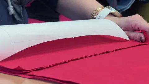 Woman prepares fabric pattern on red textile surface for crafting project Stock Footage 342156725