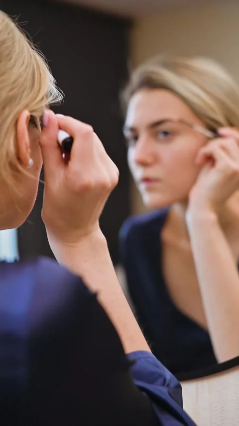 A woman prepares her look while applying makeup in front of a mirror. The focus Stock-Footage 337555520