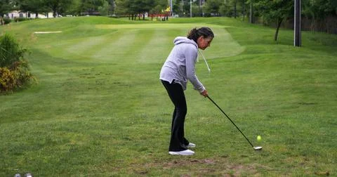 Woman Preparing to Hit Golf Ball on Green Course in Sunlight 스톡 사진