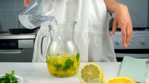 Woman preparing homemade lemonade adding water to citrus fruit herbs in jug. Stock Footage 313120398