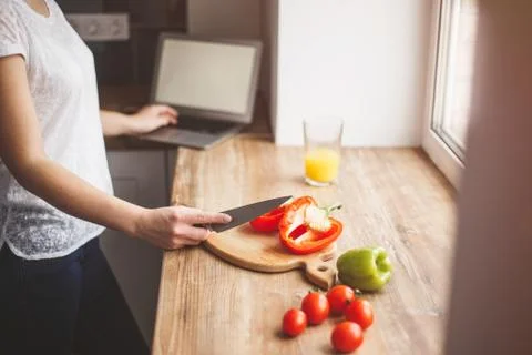 A woman is preparing a meal and working on a laptop. Nearby is a glass of jui Stock Photos