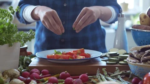 Woman preparing salad adding basil to sliced tomatoes in kitchen Stock Footage 70108621