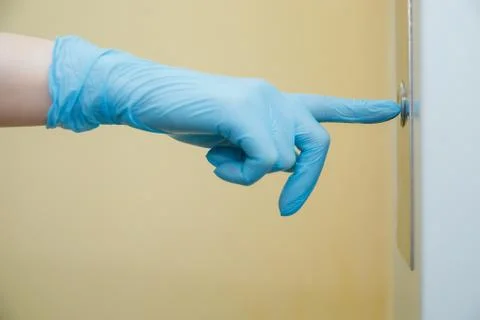 Woman presses elevator button in protective medical glove. Concept coronavirus Stock Photos