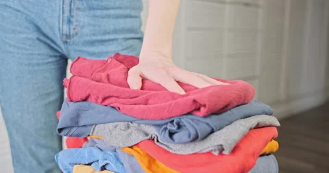 Woman presses folded stack of clothes with her hand. Close-up, indoors. Concept Stock Footage 235343476