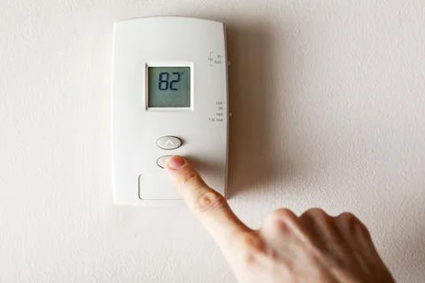 A woman is pressing the down button of a wall attached house thermostat with  Stock Photos
