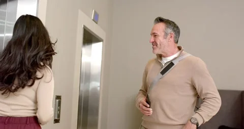 Woman pressing elevator button in lobby, man smiling and gesturing her inside as Stock Footage 317660675