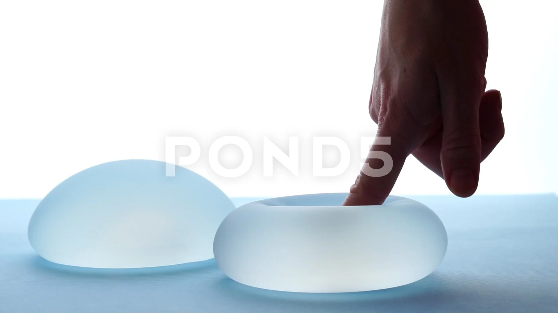 Woman pressing soft round breast implant in backlight. Plastic surgery