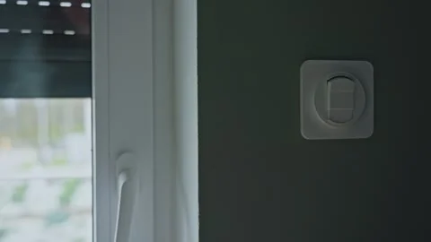 Woman pressing wall switch while exterior roller shutter goes down Stock Footage 331602957