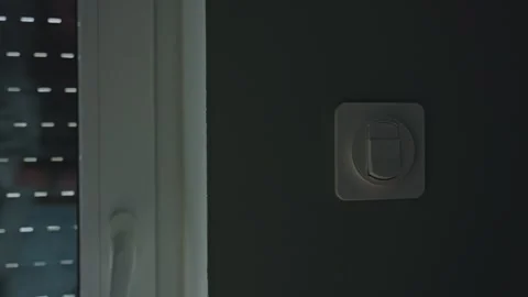 Woman pressing wall switch while exterior roller shutter goes up on window 库存影片 331750927
