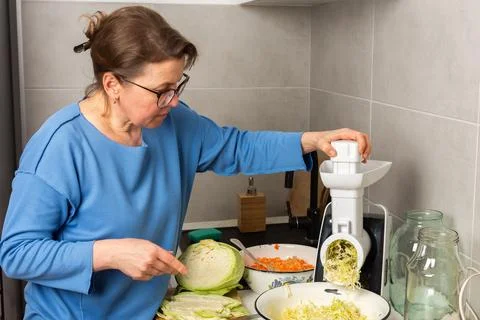 A woman processes cabbage in her kitchen using a food processor. She focuses  Stock Photos