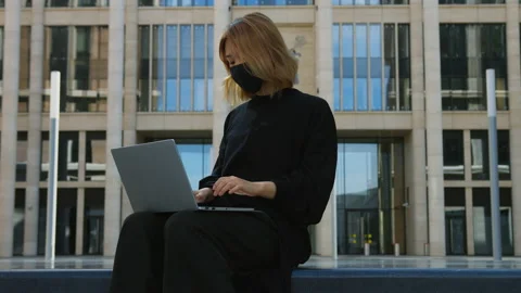 Woman in protective face mask types on laptop keyboard sitting on bench Stock Footage 157388965
