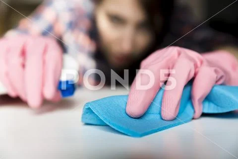 Woman in protective gloves is diligently cleaning white surface using a spray Stock Photos