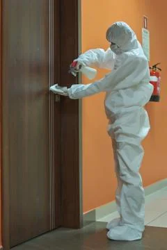 A woman in a protective suit disinfects door handles, coronavirus pandemic Stock Photos