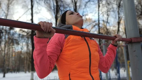 Woman is pulling herself on a horizontal bar outdoors in the park in winter. Video stock 124467874