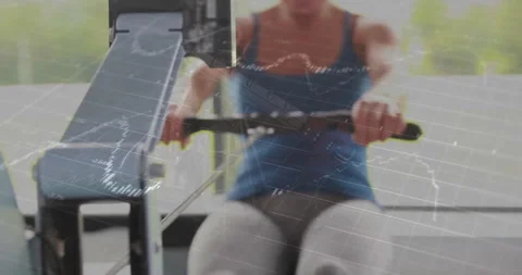 Woman pulling rowing machine handle while financial stock charts floating across Stock Footage 307550934