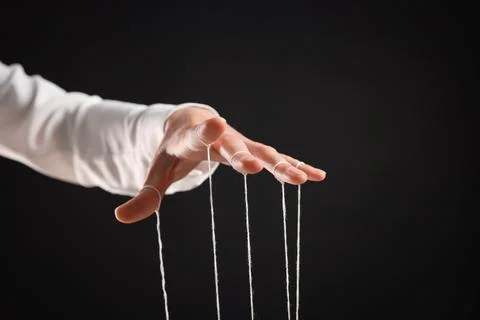 Woman pulling strings of puppet on black background, closeup Stock Photos