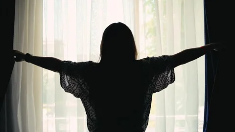 The woman pulls back the curtains and opens the morning light inside. Stock Footage 323442122