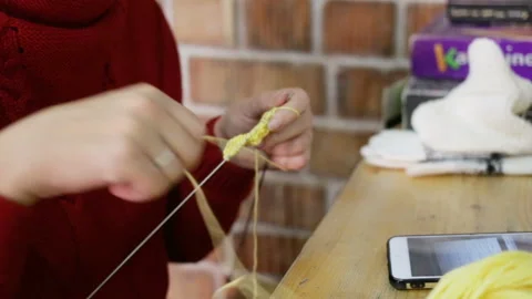 A woman pulls a ball of thread, she knits a yellow baby bootie. On the table are Stock Footage 144110085