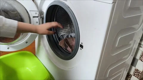 A woman pulls clean laundry out of a washing machine. Stockbeeldmateriaal 311992607
