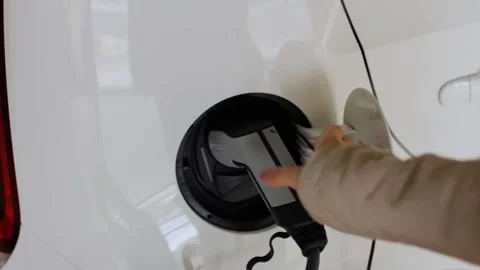 A woman pulls out a plug from the car socket at the public charging station Stock Footage 134491649