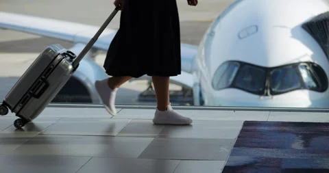 Woman pulls small suitcase as she walks through terminal, passing by window Stock Footage 283478051