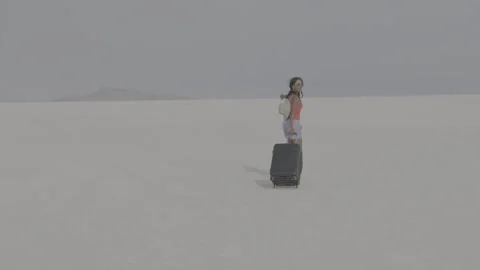 Woman pulls suitcase through vast empty desert landscape on a sunny day Stock Footage 312646706