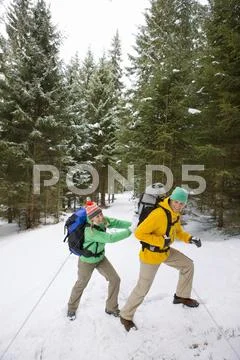 Woman Pushing Man With Backpack Up Snowy Slope In Woods