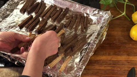 A woman puts pieces of rye bread on a baking tray to make breadcrumbs 库存影片 301245602