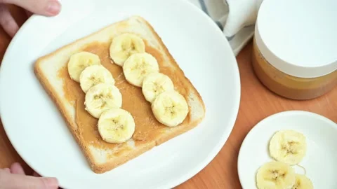 A woman puts a plate of crispy peanut butter and banana toast on a wooden table. Stock Footage 143634341