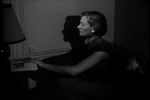 Woman puts plug of lamp in socket and reads a book - 1953 Stock Footage 106189348
