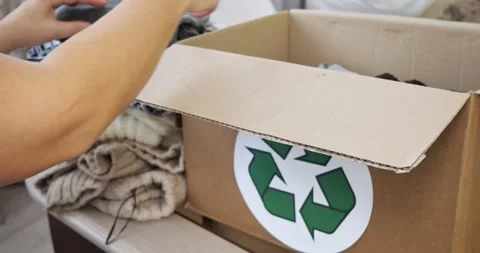 A woman puts a stack of items into a cardboard box for donation or recycling Stock Footage 267736953