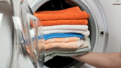 Woman puts a stack of laundry in the washing machine Stock Footage 107078145