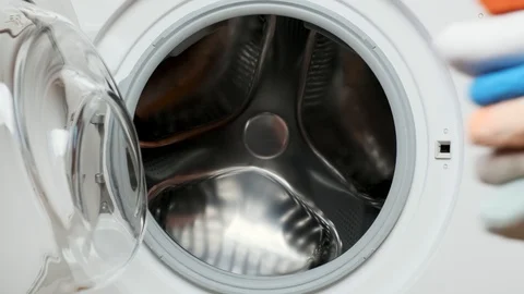 Woman puts a stack of laundry in the washing machine Stock Footage 107078203