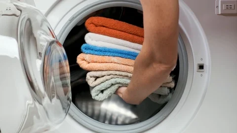 Woman puts a stack of laundry in the washing machine and closes the door. Stock Footage 107329961