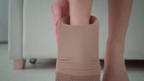 Woman putting on compression stocking using assist device at home Stock Footage 321708240