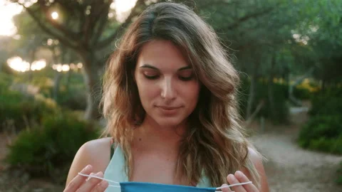 Woman Putting On A Face Mask While Looking Straight At The Camera Stock Footage 136594124