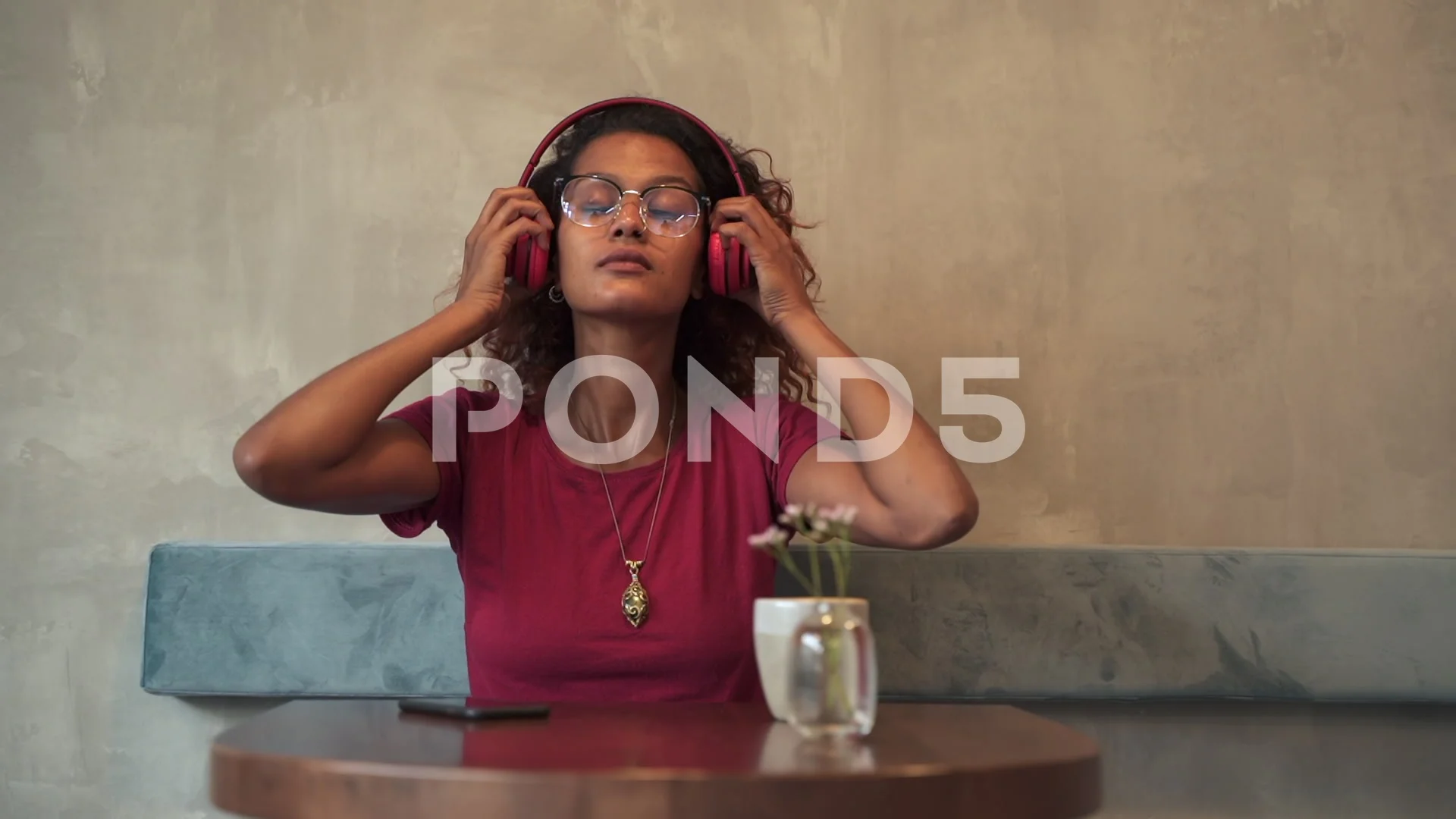 Woman putting on headphones and listening to music with phone sitting at table