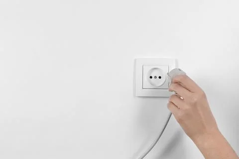 Woman putting plug into power socket on white background, closeup. Electricia Stock Photos