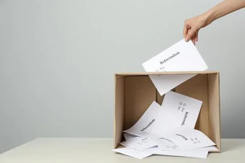 Woman putting referendum ballot in box on table against light grey background Stock Photos