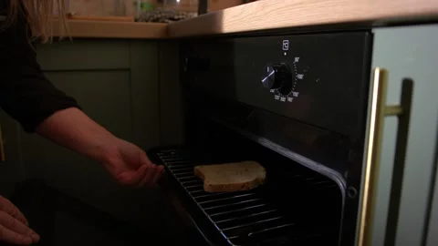 Woman putting slice of bread in oven grill to make toast 動画素材 346720746