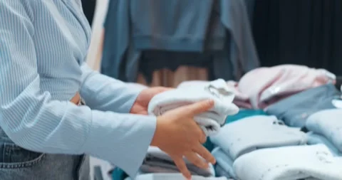 Woman putting things back in stack in clothing store. Woman tries on clothes Stock Footage 257927178
