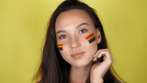 Woman with a rainbow pattern on her face. The woman looks into the camera Video stock 137014527