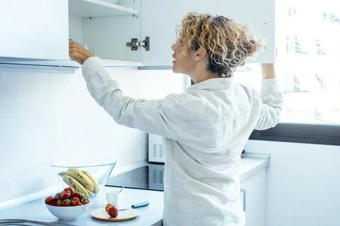 Woman reaching into kitchen cabinet in bright modern kitchen with fruit bow.. Stock-Fotos