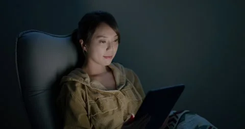 Woman read on tablet computer and sit on the chair at night inside the room Video stock 188952568