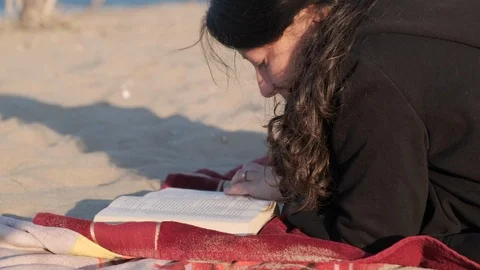 Woman reading a book on the beach during sunset wearing sweatshirt. Left side Stock Footage