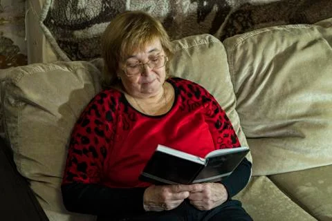 A woman is reading a book sitting on the couch. Stock Photos