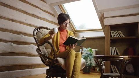 Woman reading book while drinking coffee on attic Stock Footage 100285444