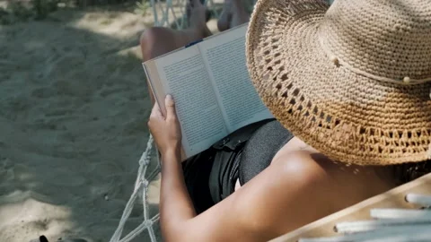 Woman reading a book while in a hammock and palm shadow on the hat Stock Footage 234963429
