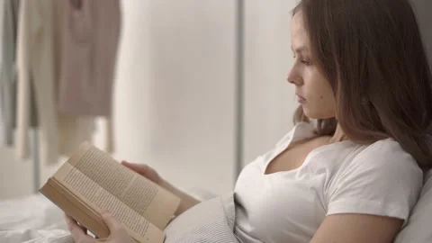 Woman reading a book while lying in bed Stock Footage 132047525