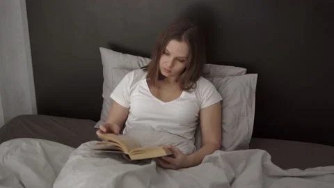 Woman reading a book while lying in bed Stock Footage 132049244